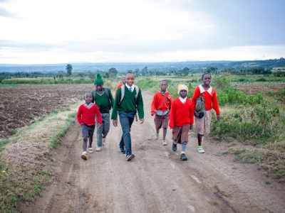 group of children in school uniforms walking on a dirt road