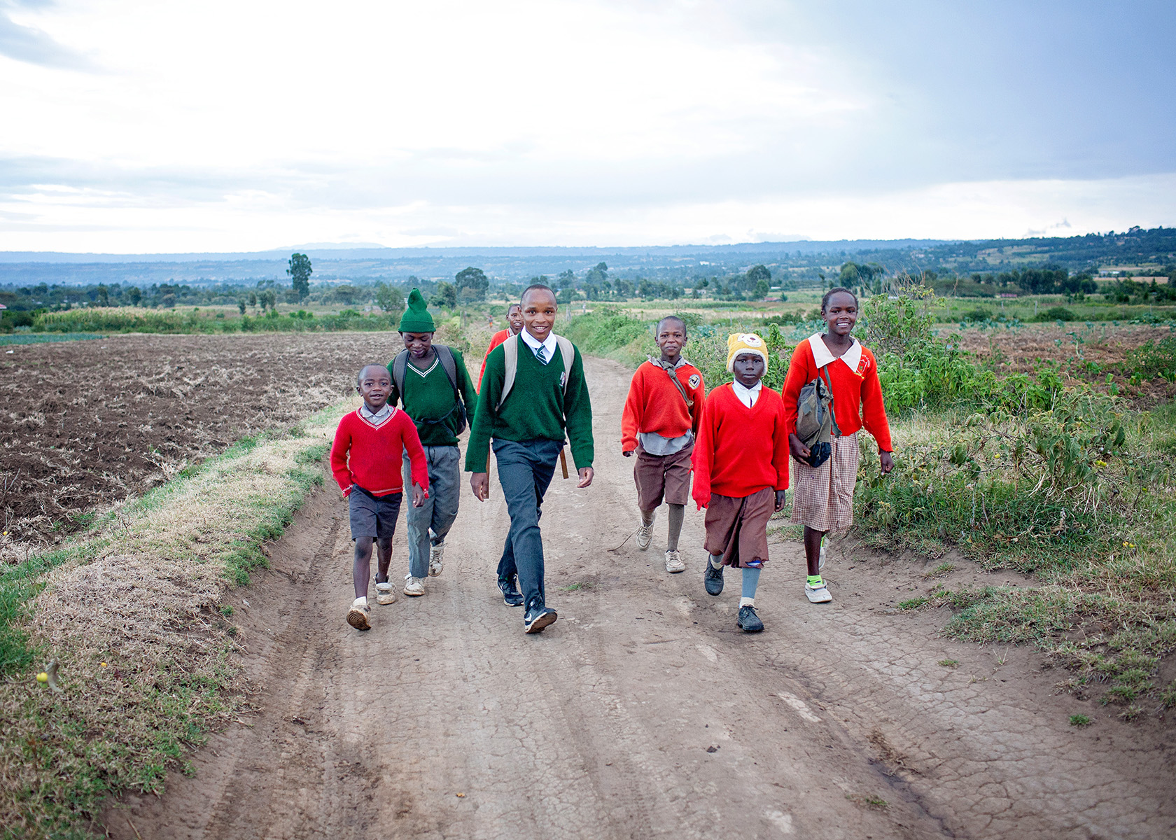 group of children in school uniforms walking on a dirt road